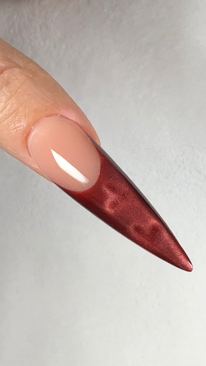 Close-up of a long, pointed nail with a red-brown color on a plain background